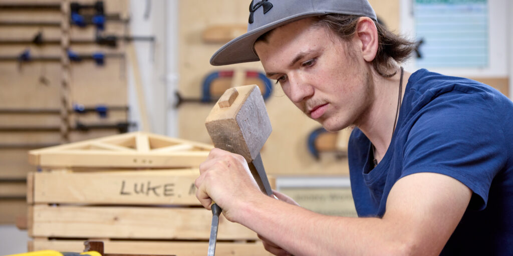 Photo of a student using a mallet and chisel in a woodworking classroom