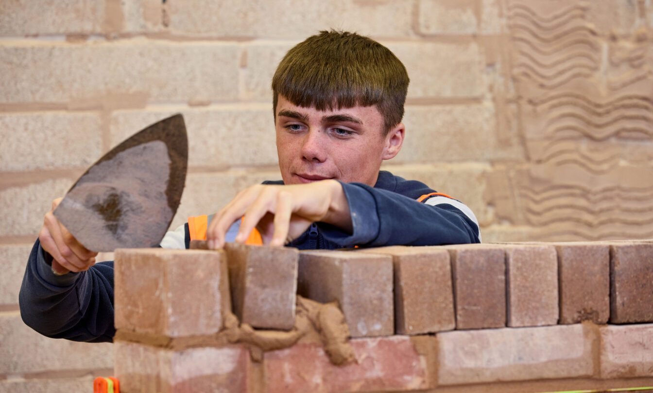 Photo of a student using a trowel to build a brick wall