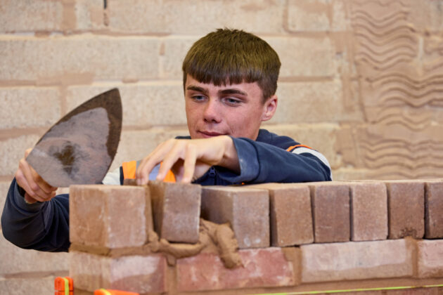 Photo of a student using a trowel to build a brick wall