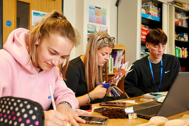 Three students sat at a table doing arts and crafts