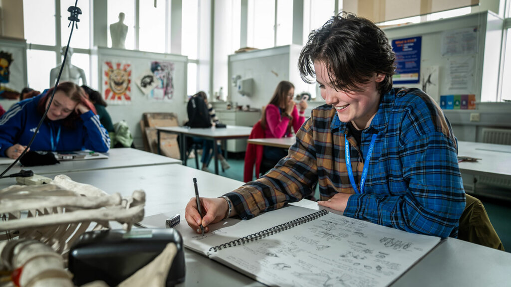 A smiling student sat at a table drawing