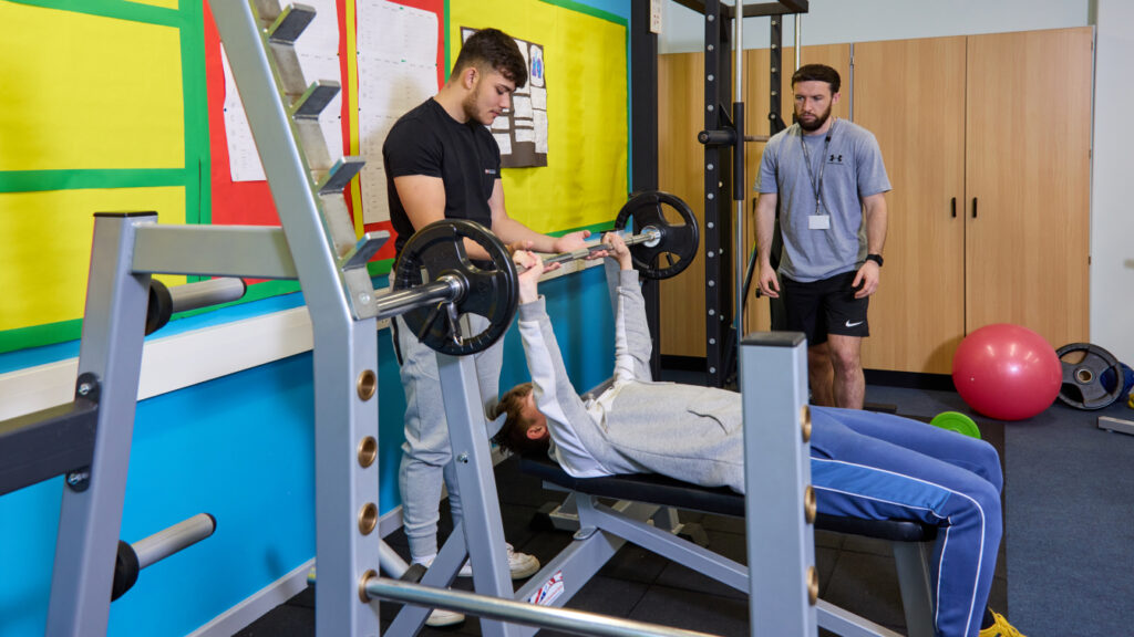 Photo of students using gym equipment while been supervised by a tutor
