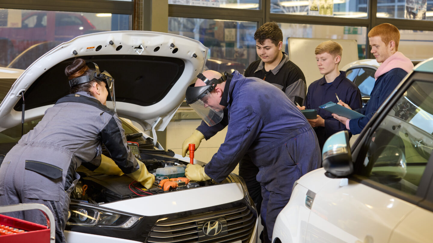 Motor vehicle students with tutor working on a car engine