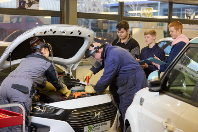 Motor vehicle students with tutor working on a car engine