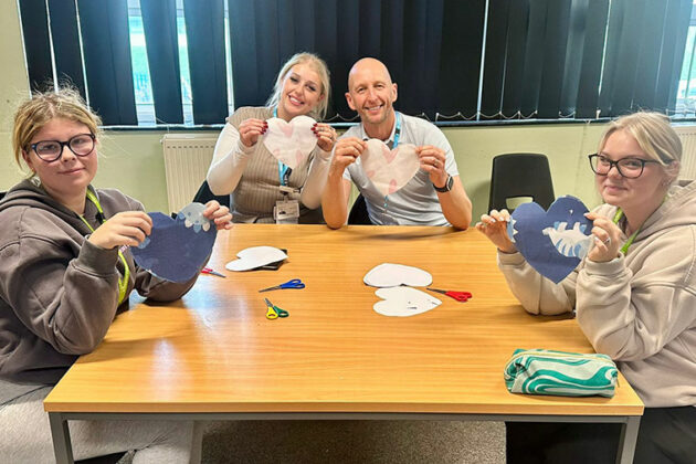 Four people sat around a table holding up hearts that they have made