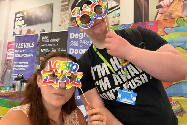 Two people holding up rainbow coloured cardboard glasses up to their faces