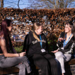 Three students sat on a wall chatting together