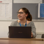 A smiling female sat at table with an open laptop